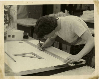Cory Betts, University of Idaho student, drafting with a pen, ruler, and a set square ruler. Seems to be part of an architecture class.