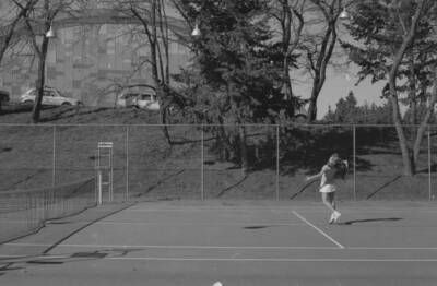 A student playing tennis on the courts just outside of the Physical Education Building.