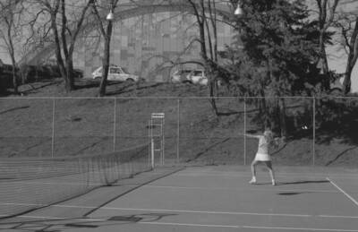 A student playing tennis on the courts just outside of the Physical Education Building.
