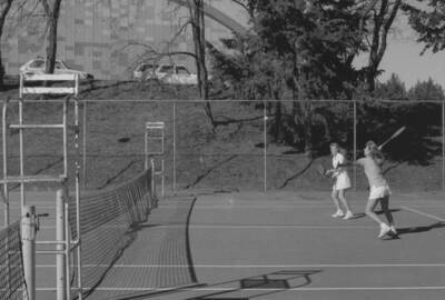 Two students playing tennis on the courts just outside of the Physical Education Building.