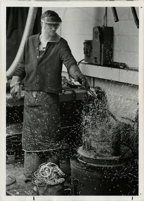A man doing some type of metal working  with sparks or particles flying all over the area.