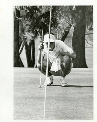 U of I Golf Course. Man analyzing the distance to the hole while crouching with a golf ball in his mouth.