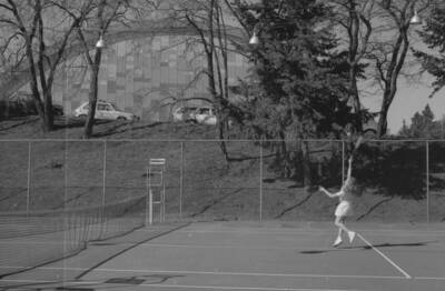 A student playing tennis on the courts just outside of the Physical Education Building.