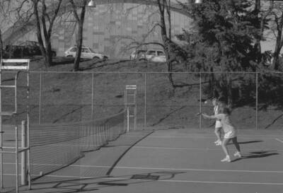 Two students playing tennis on the courts just outside of the Physical Education Building.