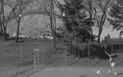 A student playing tennis on the courts just outside of the Physical Education Building.