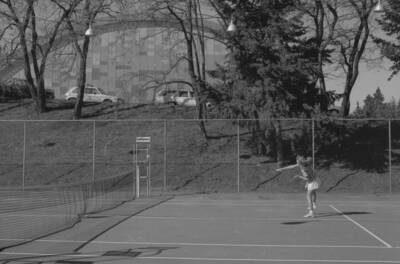A student playing tennis on the courts just outside of the Physical Education Building.