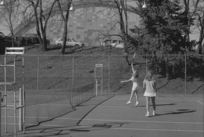Two students playing tennis on the courts just outside of the Physical Education Building.