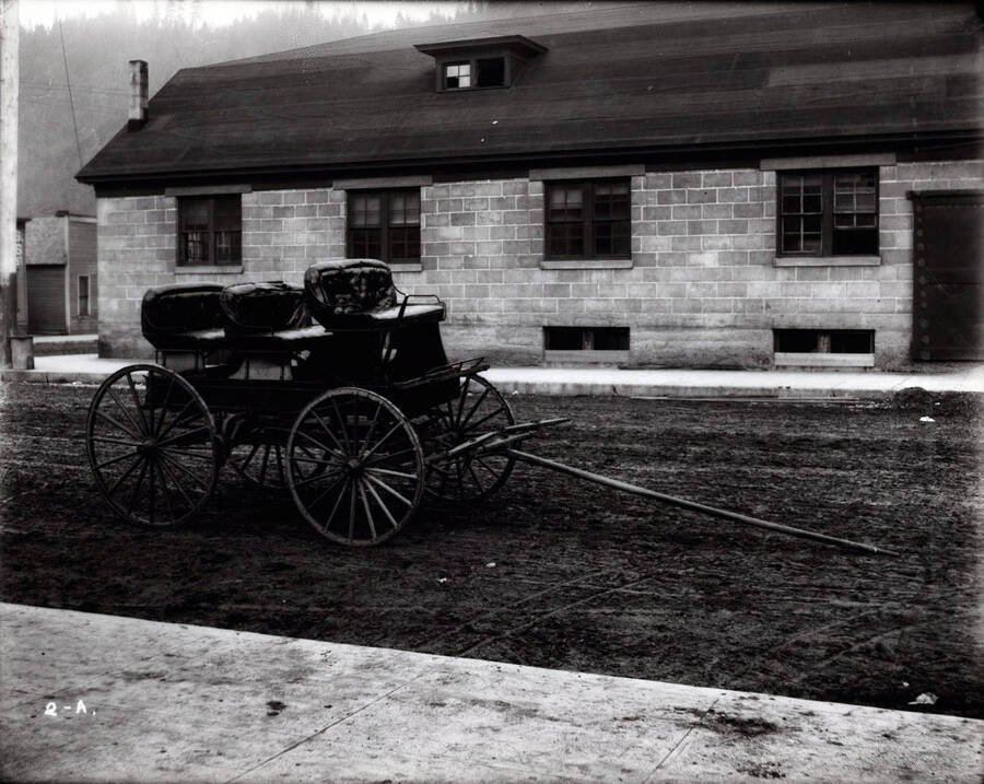 Image shows Henry Floyd Samuels horse drawn carriage located on a muddy road with a building in the background.