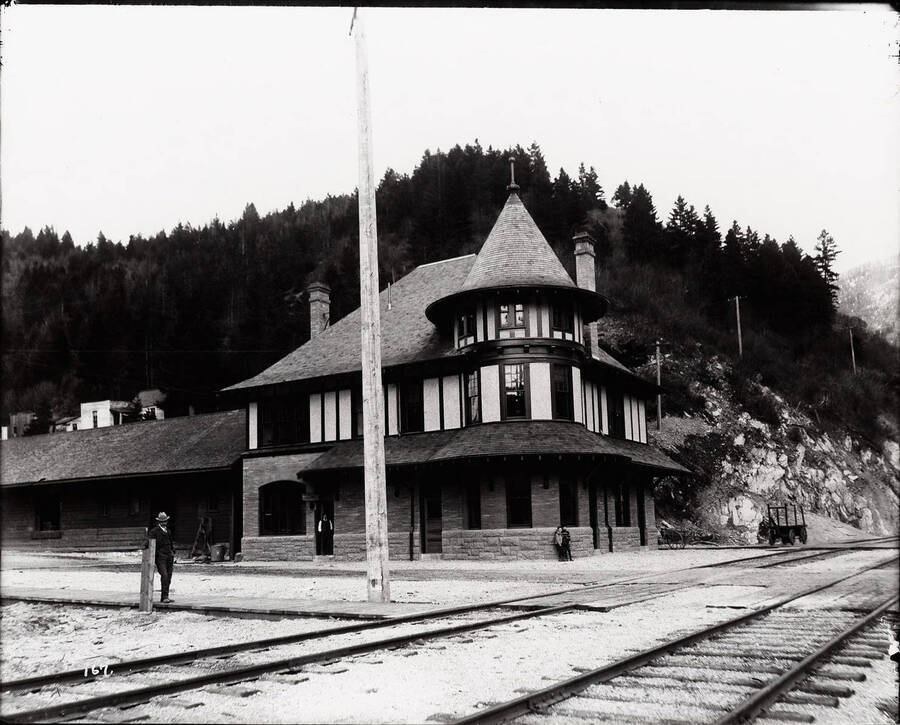 Front view of the Northern Pacific Railroad depot on the north end of 6th Street in Wallace, Idaho. Caption on Back: "Depot has a prominent corner turret, was built for $8,330 by the Northern Pacific Railroad ("as per plan 281-1" according to company records) with brick from China. The brick had been imported in 1890 for the Olympic Hotel in Tacoma. The hotel, burnt when only partially completed, was dismantled in 1899-1901 to provide material for the depots in Wallace and Missoula."