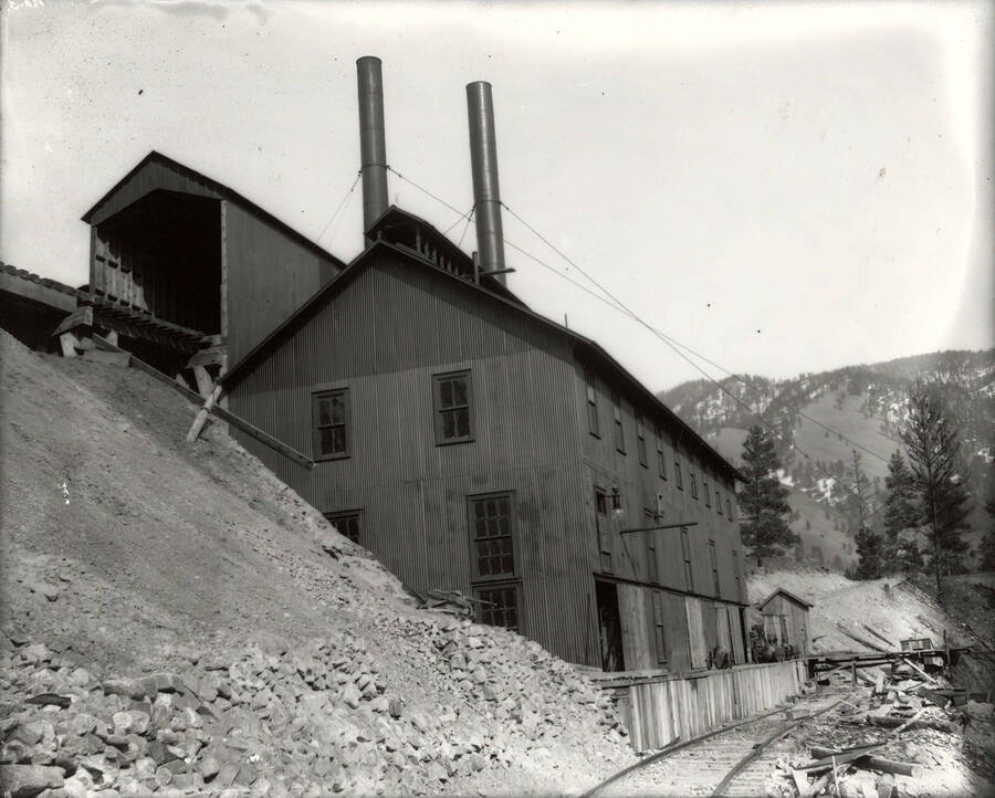 View of a large building, a covered train trestle, and lower railroad tracks at the Amador Mine in Cedar Creek, Montana.