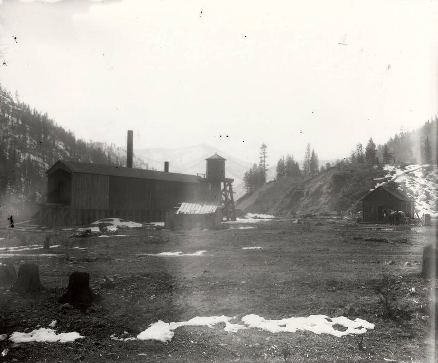 View of the back side of a large building at the Amador Mine in Cedar Creek, Montana. In the distance (on the left) there is a horse being hitched to a wagon.