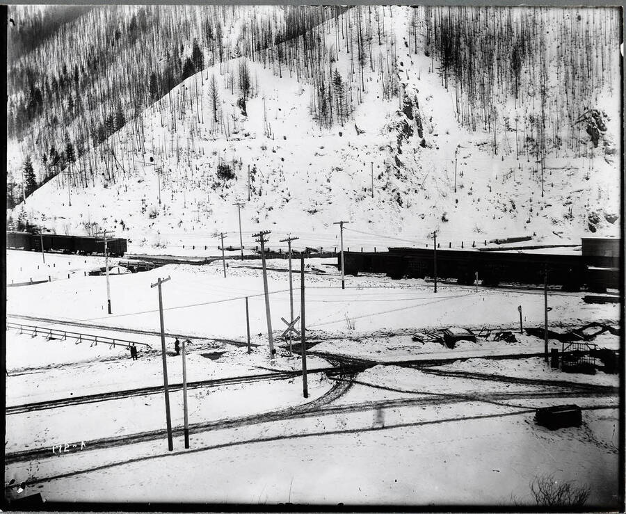 Oregon, Washington Railroad & Navigation Company accident photograph. This distant view shows snow covered tracks with two men standing to the left side. Caption on front: "O.W.R. and N. Accident Case, 1913 Edge of Wallace."