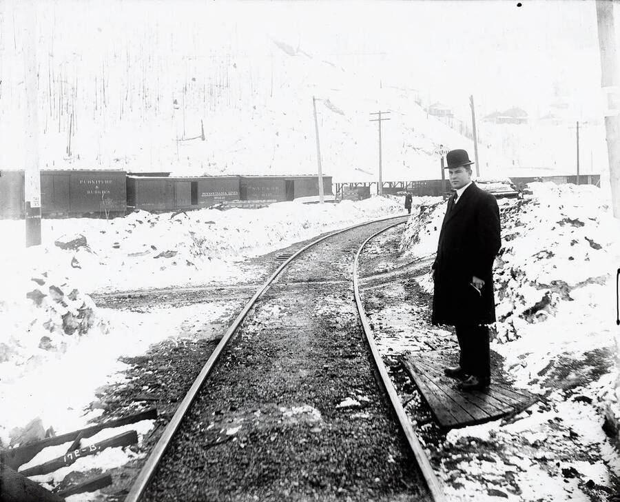 Close-up of a man  standing next to some Oregon, Washington Railroad & Navigation Company  tracks. Caption on front: "O.W.R. and N. Accident Case, 1913 Edge of Wallace."