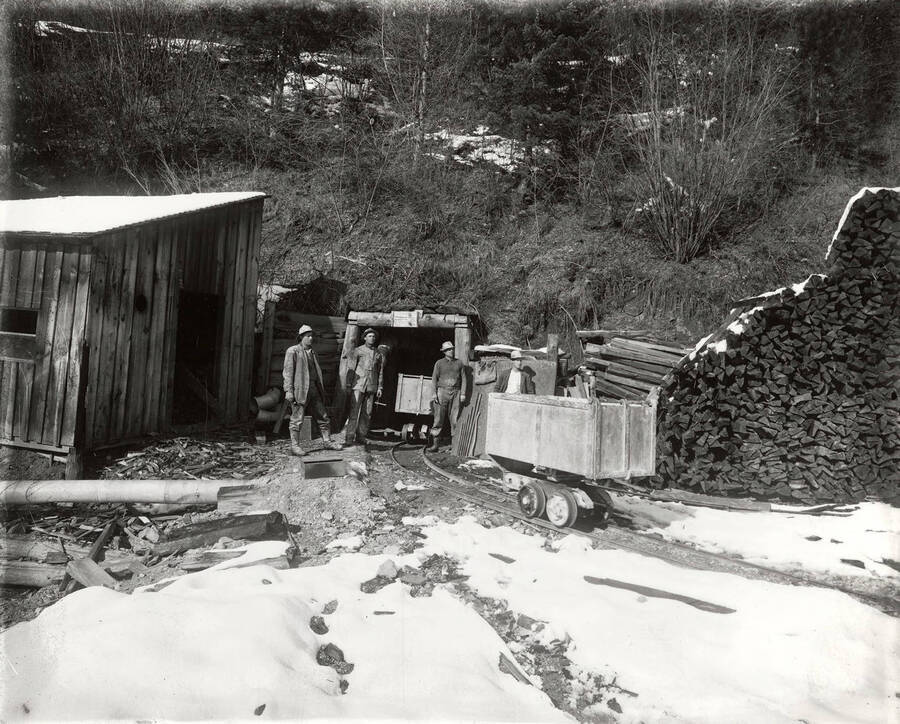 Four men standing with a cart at the entrance to a tunnel on Hector Mine.