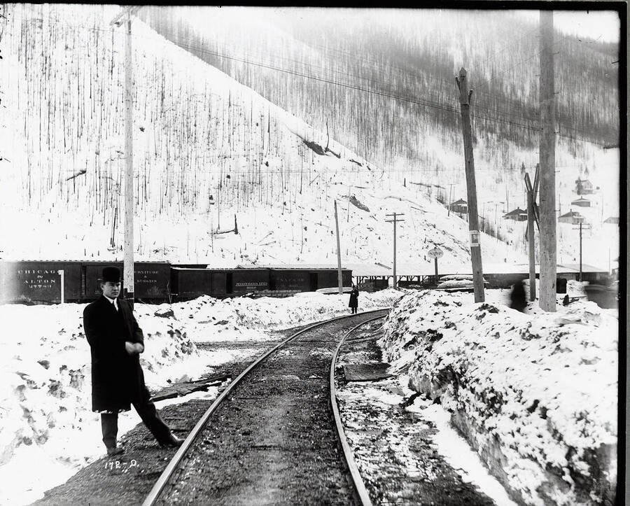 Close-up of a man  standing next to some Oregon, Washington Railroad & Navigation Company  tracks, with another man in the distance. Caption: "O.W.R. and N. Accident Case, 1913 Edge of Wallace."