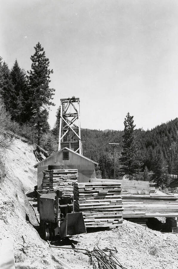 Exterior view of Thomas Mines in Wallace, Idaho. Equipment and stacked wood can be seen.