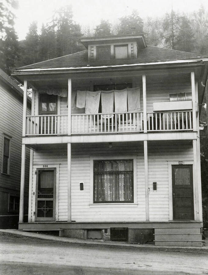 View of a two-story house in Wallace, Idaho with a towels hanging on a clothesline on the second floor balcony. A real estate view taken for Idaho First National Bank.