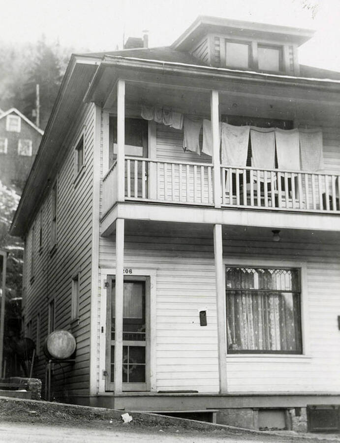View of a two-story house in Wallace, Idaho with a towels hanging on a clothesline on the second floor balcony. A real estate view taken for Idaho First National Bank.