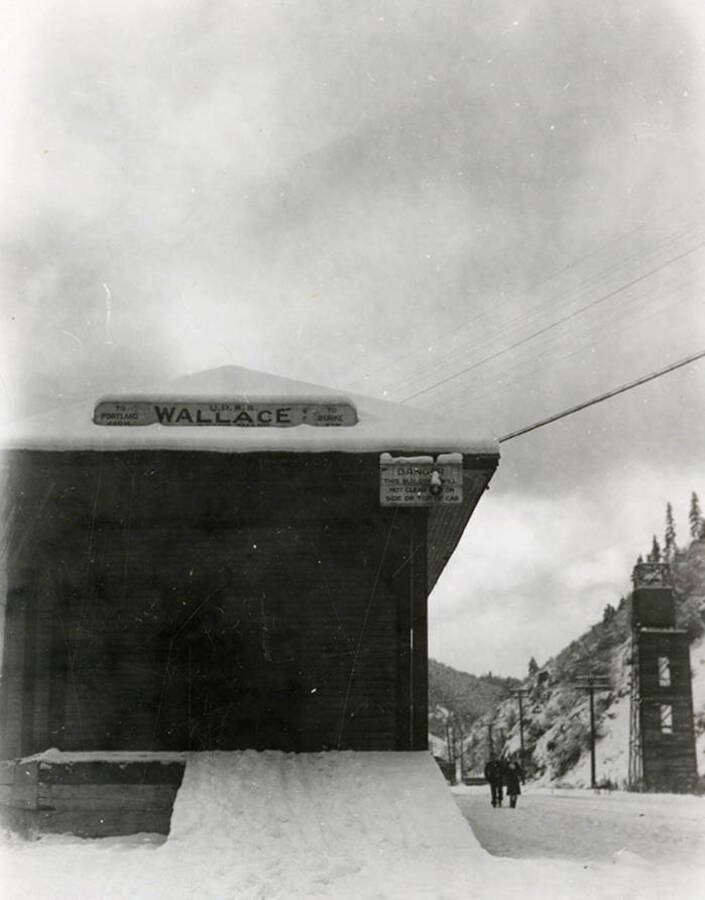 The Union Pacific Railroad Station covered in snow. People can be seen walking by the station. Located at the end of Baker Street in Wallace, Idaho.