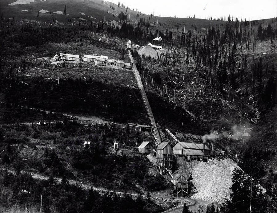 Hercules Mine in Burke, Idaho. Image features several wooden structures on multiple levels. Two large dump piles can be seen at separate levels.