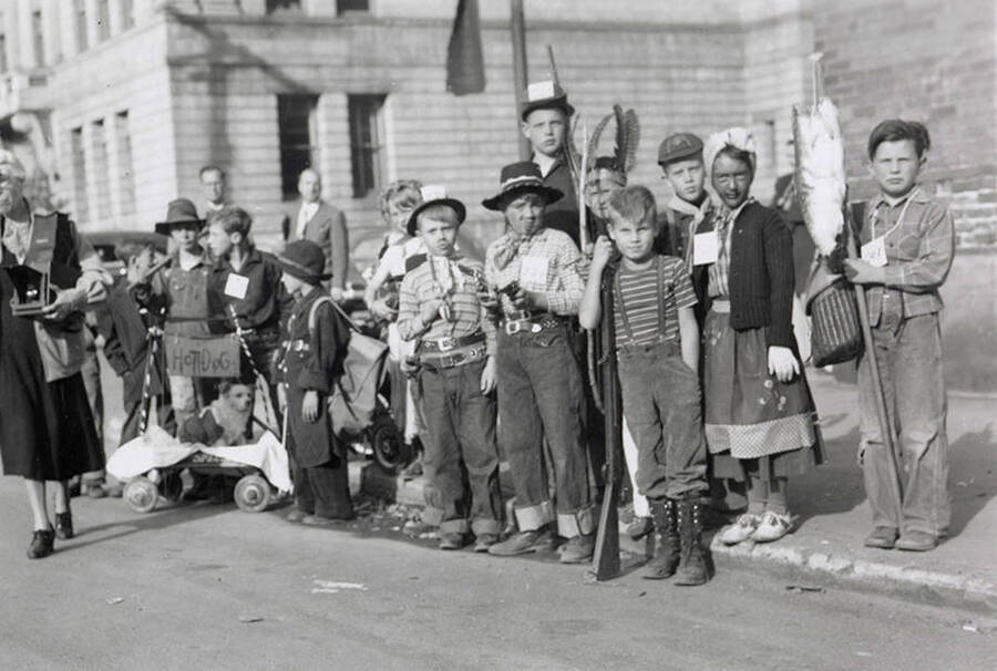 Children standing on the sidewalk during the Elks Roundup parade in Wallace, Idaho. Nellie Stockbridge (1868-1965) can be seen on the right.