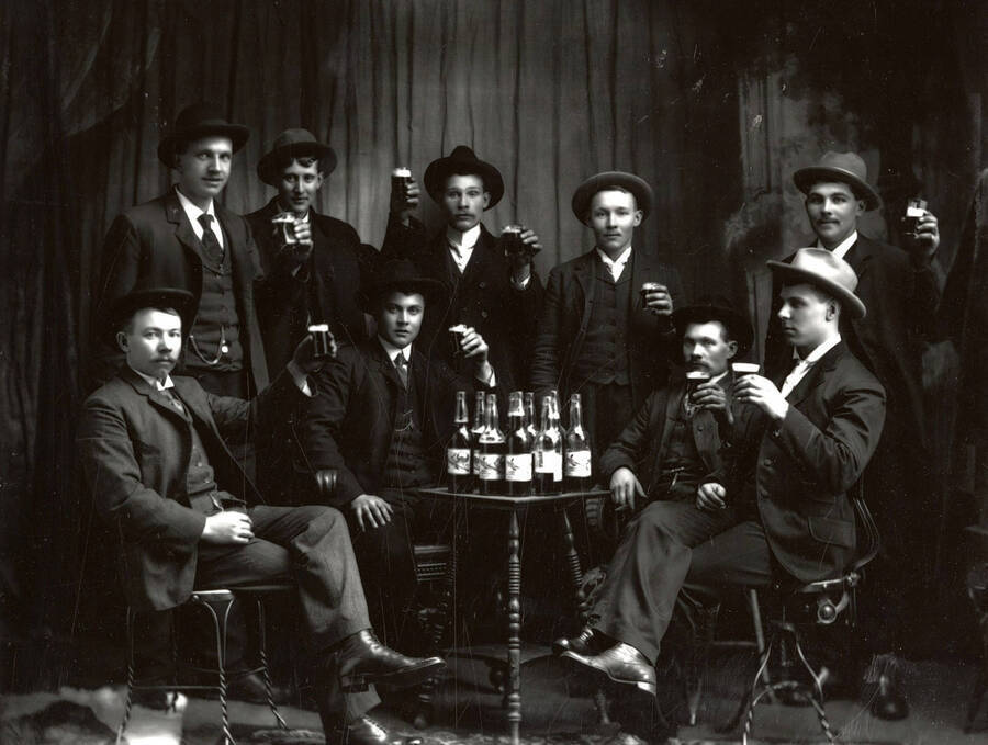 The men of the Vic Strong Group each holding up a beverage glass and sitting around a table with drinks.