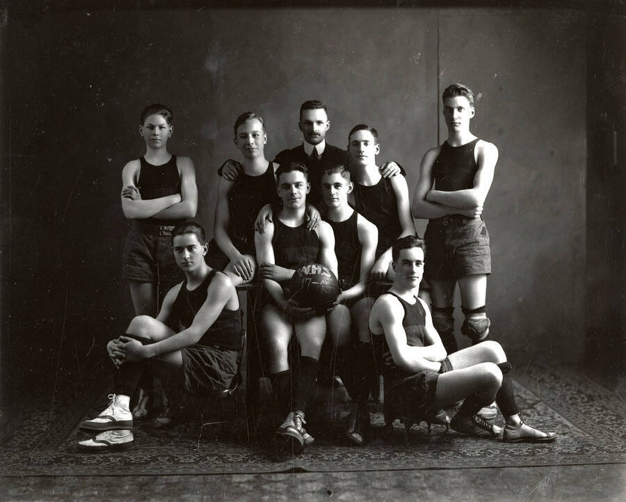 Eight boys, who were part of the Wallace High School Basketball team, posing in their basketball uniforms with the coach.