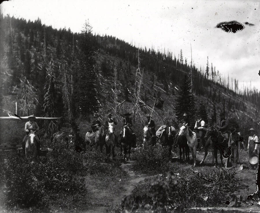 Eight men on horseback surrounded by trees.