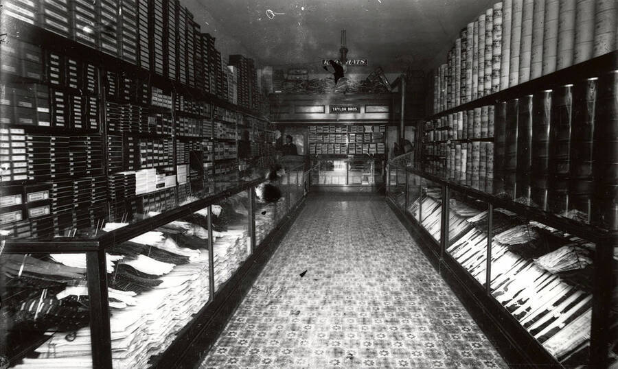 Interior view of the Taylor Bros. Clothing Store in Wallace, Idaho. Shelves, hat boxes, other boxes, and show cases line the walls.