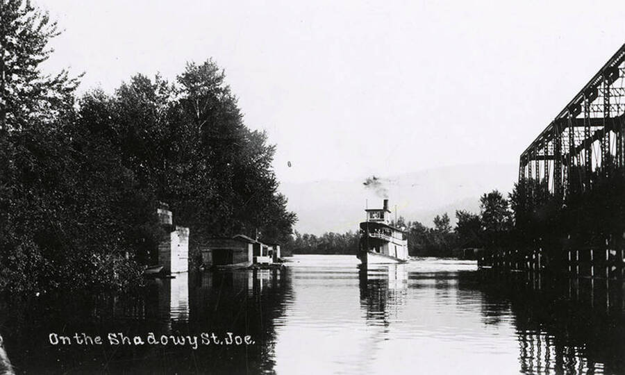 Steamboat "Spokane" on the St. Joe River, with trees along the bank and a bridge.