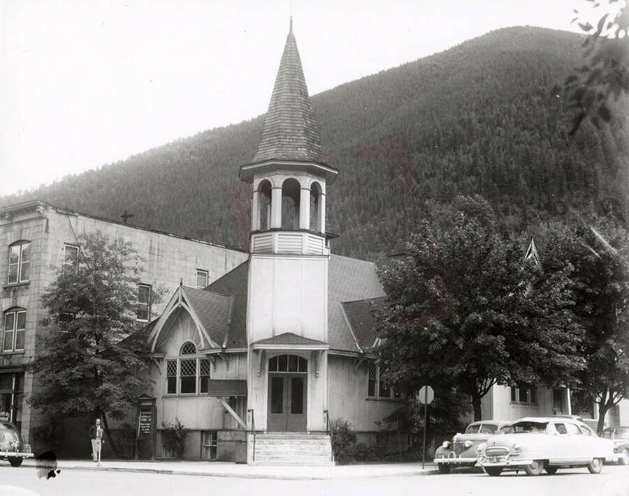 Exterior view of the Congregational Church in Wallace, Idaho. The church sits on the corner of the street, and has a few cars and a man in front of it.