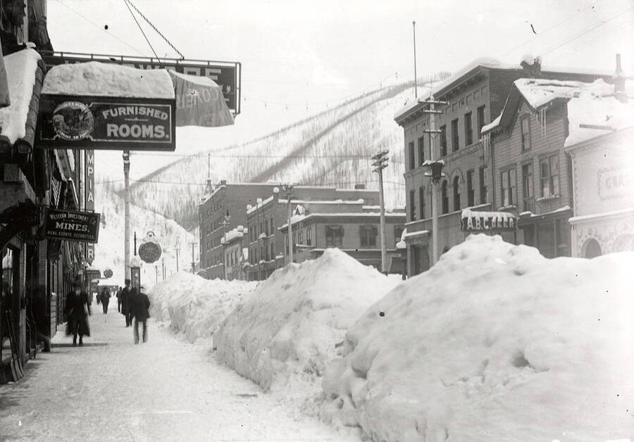 Looking down Cedar Street  during the winter in Wallace, Idaho. Residents are walking next to buildings in the snow.