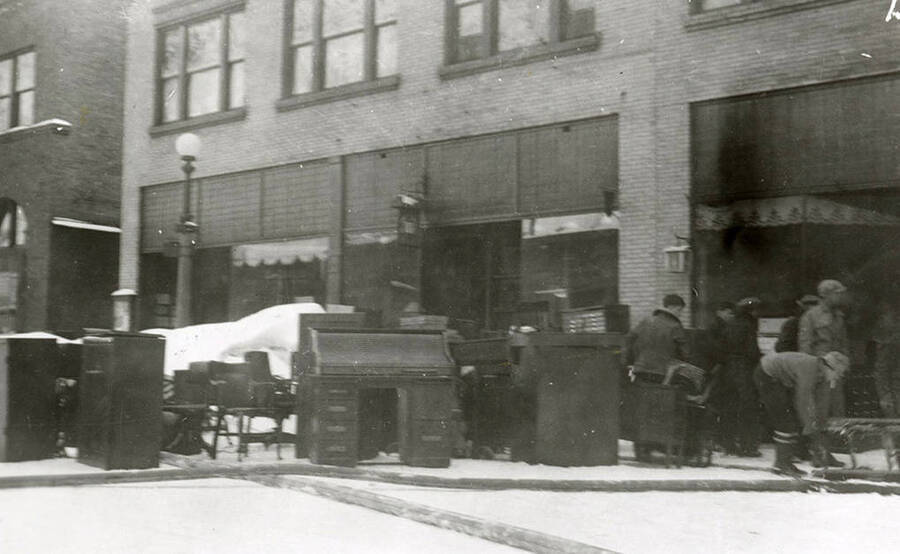 View of the fire at the Ryan Hotel on Cedar Street in Wallace, Idaho. People are standing on the street out front with the furniture.