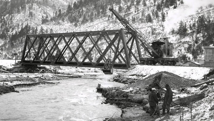 View of the railroad bridge at the west city limits of Wallace, Idaho during the Placer Creek Flood. The bucket dredge can be seen at work.