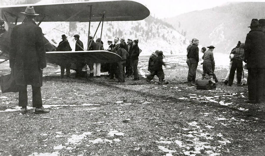 View of airport during the Placer Creek Flood in Wallace, Idaho. A group of people can be seen standing near and airplane.