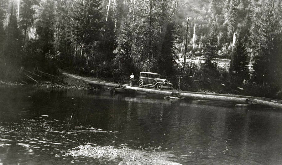 A man and a car parked on a bridge, with trees in the background, near Delta, Idaho.