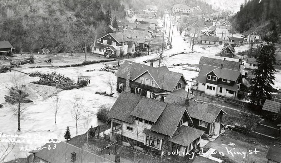 Looking down King Street during the Placer Creek flood in Wallace, Idaho. Houses line the street and Our Lady of Lourdes Academy can be seen in the background.