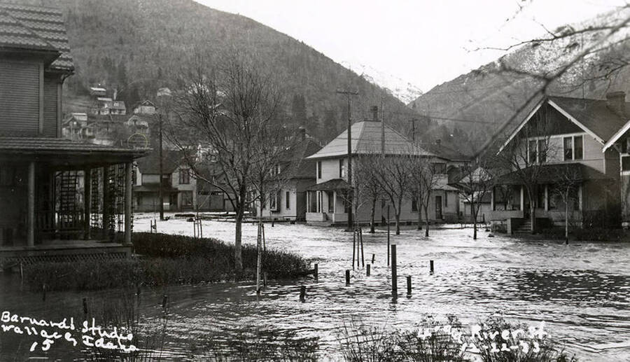 View of Fourth and River Street during the Placer Creek flood in Wallace, Idaho. Houses line the street and a hill can be seen in the distance.