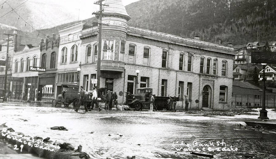 View of Sixth and Bank Streets during the Placer Creek flood in Wallace, Idaho. People can be seen walking on the sidewalks.