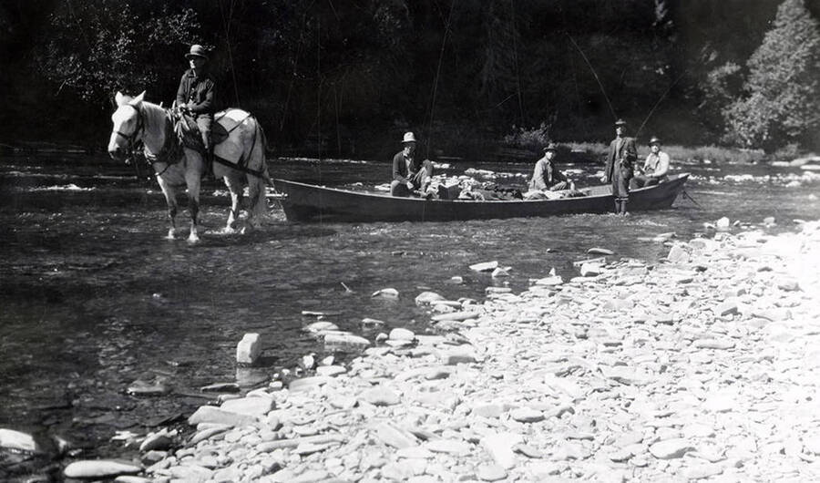 Men sitting in a boat and fishing on the North Fork. One man is sitting on a horse in front of the boat.
