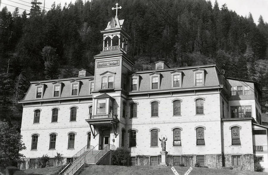 Exterior view of the Providence Hospital in Wallace, Idaho. A mountain covered in trees can be seen in the background.