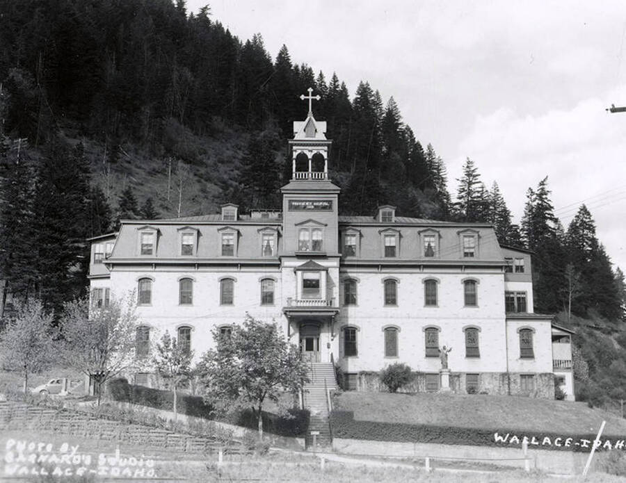 Exterior view of the Providence Hospital in Wallace, Idaho. A mountain covered in trees can be seen in the background.