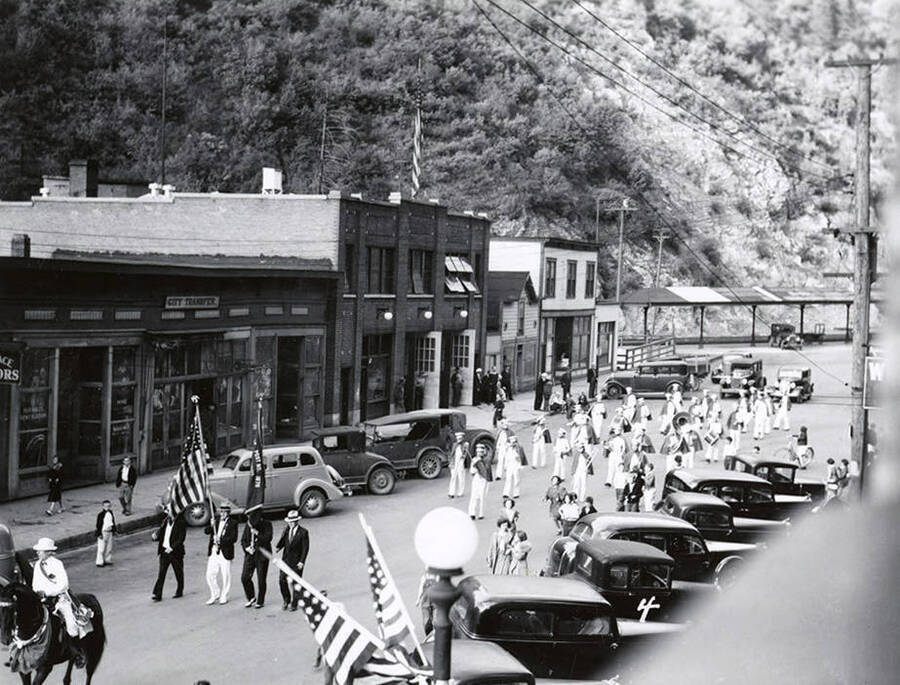 The band marching in the Elks Roundup parade in Wallace, Idaho. Cars line the streets.