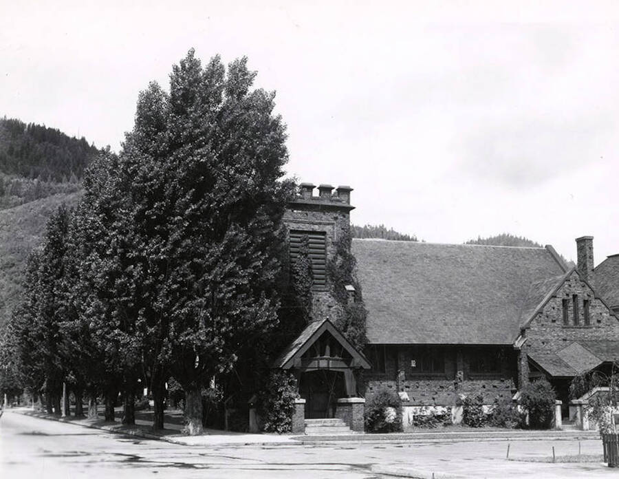 Exterior view of the Holy Trinity Episcopal Church in Wallace, Idaho. The church is on the corner of a street and trees line the church on one side.