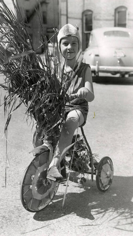 A child, who is in costume, riding a bicycle in the Fourth of July Parade in Wallace, Idaho.
