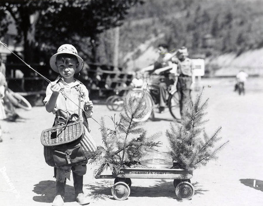A boy, holding and fishing rod and standing next to a wagon, during the Wallace pet parade in Wallace, Idaho.