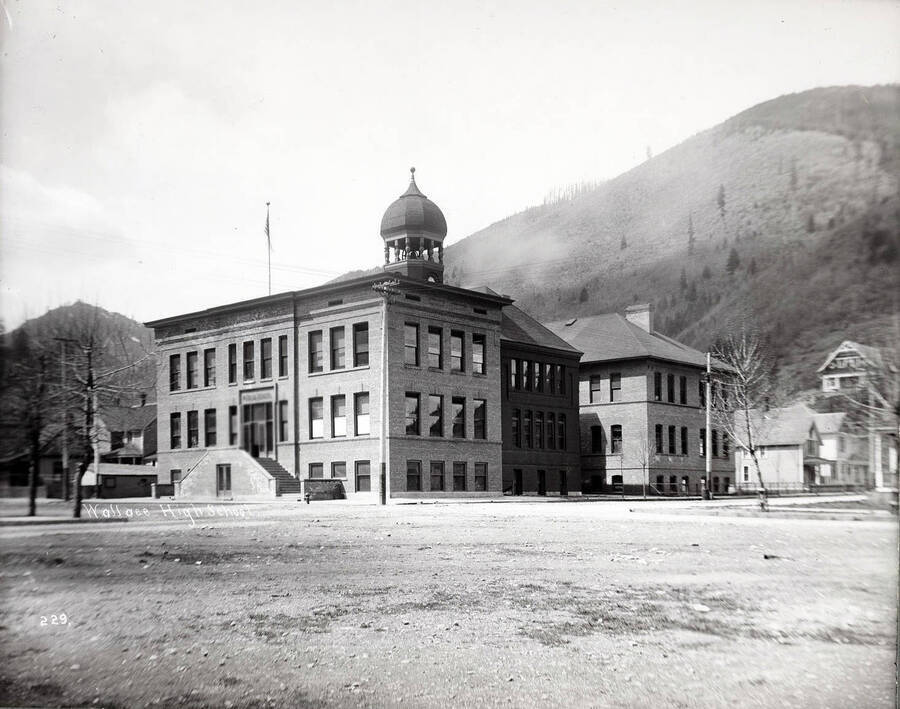 Image of the outside of the Wallace High School, before the awning covering the front steps was added. Caption on front: "Wallace High School."