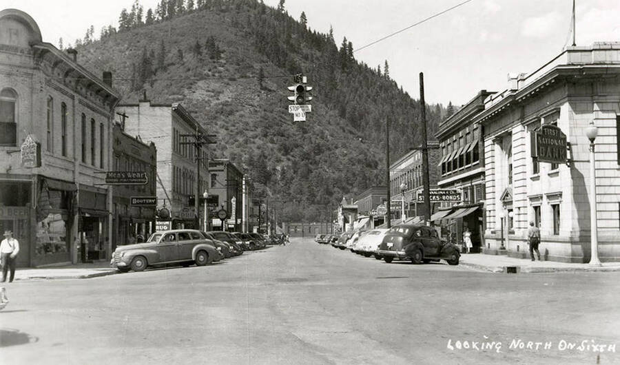 Looking north on 6th Street in Wallace, Idaho. Cars are parked in front of stores, which line the street.