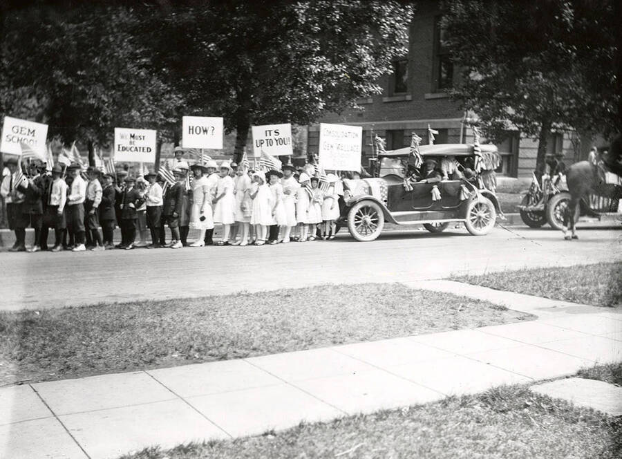 Children carrying signs about school consolidation of the Gem and Wallace school districts during the Fourth of July Parade in Wallace, Idaho.