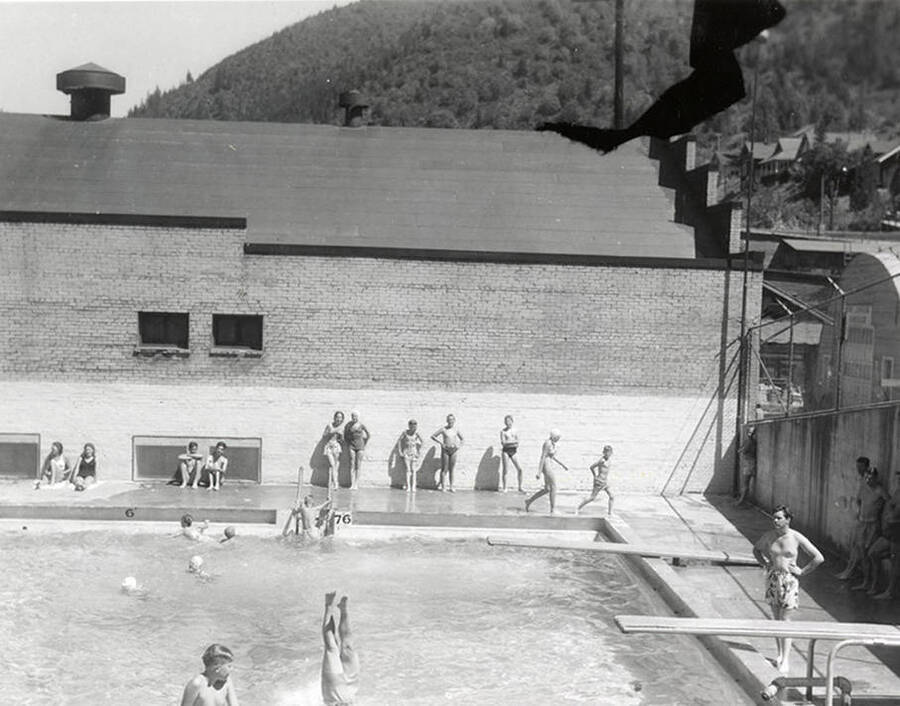 Jack Foster diving in the swimming pool in Wallace, Idaho. Others stand around the pool, watching.